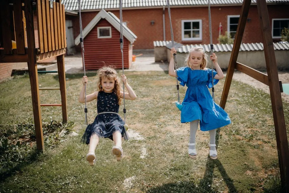 Two children playing on swings in a sunny backyard, illustrating the kind of unstructured time kids need covered during school breaks.